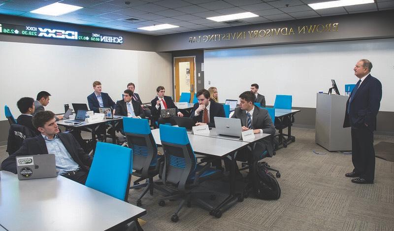 Eleven formally-dressed students work in the Brown Advisory Investing Lab under the supervision of an older advisor.